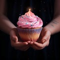 Woman holding a multicolored creamy cupcake in hands with a candle on top, close up. Woman\'s hands holding pink cupcake