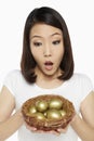 Woman holding a nest filled with gold eggs, looking shocked