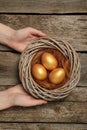 Woman holding nest with shiny golden eggs at wooden table, top view Royalty Free Stock Photo