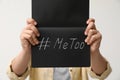 Woman holding notebook with hashtag MeToo against light background. Stop sexual assault