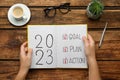 Woman holding notebook with text 2023 Goal, Plan, Action at wooden table, top view. New Year resolutions Royalty Free Stock Photo