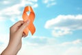 Woman holding orange ribbon against blue sky, closeup with space for text. Multiple sclerosis awareness Royalty Free Stock Photo