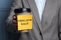 Woman holding paper coffee cup with Welcome Back sticky note, closeup Royalty Free Stock Photo