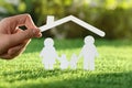 Woman holding paper roof over cutout of family on fresh grass, closeup. Life insurance Royalty Free Stock Photo