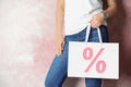 Woman holding paper shopping bag with percent sign near pink wall, closeup. Discount concept