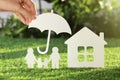 Woman holding paper umbrella over cutout of family and house on fresh grass, closeup. Royalty Free Stock Photo