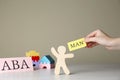 Woman holding paper with word Man near human figure and abbreviation ABA Applied behavior analysis at white wooden table,