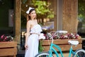 Woman holding peonies near vintage bicycle against terrace of cafe Royalty Free Stock Photo