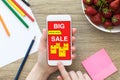 Woman holding phone with big sale on screen over table