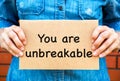 Woman holding a piece of a cardboard with words You Are Unbreakable