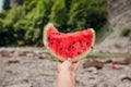 Woman holding piece of watermelon in hand on mountain background. Snacks during traveling in summer