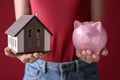 Woman holding piggy bank and house model on color background Royalty Free Stock Photo