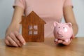 Woman holding piggy bank and house model at wooden table, closeup Royalty Free Stock Photo