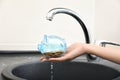 Woman holding piggy bank under metal tap. Water saving concept Royalty Free Stock Photo