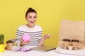 Woman holding piggybank and pointing at coffee with pizza box, looking with positive expression, Royalty Free Stock Photo