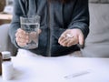 Woman holding pill and glass of water in hands sitting on a couch in the living room at home Royalty Free Stock Photo