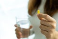 Woman holding pills or drug capsules and a glass of water in hand. Young woman take medication, feeling sick and stomach pain or t Royalty Free Stock Photo