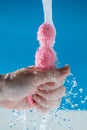 Woman holding pink anal beads under running water on blue background. Sex toy hygiene concept. Royalty Free Stock Photo