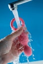 Woman holding pink anal beads under running water on blue background. Sex toy hygiene concept. Royalty Free Stock Photo