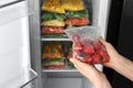 Woman holding plastic bag with frozen tomatoes near open refrigerator