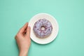 Woman holding plate with delicious glazed donut on turquoise background