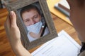 Woman holding portrait of deceased husband with improperly wearing protective medical mask closeup