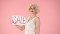 Woman holding a poster labeled Sale. Woman in look of Marilyn Monroe in studio on pink background close up. Sale, black Royalty Free Stock Photo