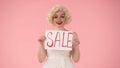 Woman holding a poster labeled Sale. Woman in look of Marilyn Monroe in studio on pink background close up. Sale, black Royalty Free Stock Photo