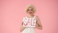 Woman holding a poster labeled Sale. Woman in look of Marilyn Monroe in studio on pink background close up. Sale, black Royalty Free Stock Photo