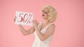 Woman holding a poster that says fifty percent. Woman looking like marilyn monroe in studio on pink background. Sale Royalty Free Stock Photo