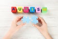 Woman holding puzzle pieces near cubes with word Autism at white wooden table, top view Royalty Free Stock Photo