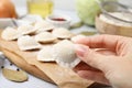 Woman holding raw dumpling (varenyk) with tasty filling at table, closeup