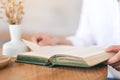 A woman holding and reading a vintage novel book on wooden table