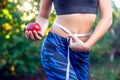 Woman holding red apple with measuring tapes on her waist outdoor. Weight loss concept. Royalty Free Stock Photo