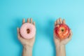 Woman holding red apple and pink donut, female choose between fruit is Healthy food and sweet is unhealthy junk foods. Dieting, Royalty Free Stock Photo