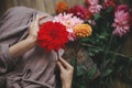 Woman holding red dahlia flower and sitting on wooden rustic bench, view above. Atmospheric moody image. Florist in linen dress