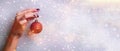Woman holding red glittering Christmas ball in hand over silver background with snow, light bokeh. Banner, copy space. New year Royalty Free Stock Photo