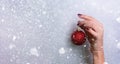 Woman holding red glittering Christmas ball in hand over silver background with snow, light bokeh. Banner, copy space. New year Royalty Free Stock Photo