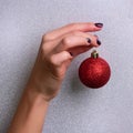 Woman holding red glittering Christmas ball in hand over silver background with snow, light bokeh. Square crop, copy space. New Royalty Free Stock Photo