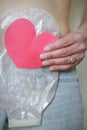 Woman holding a red heart while wearing a two piece colostomy bag