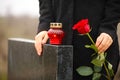 Woman holding red rose near black granite tombstone with candle outdoors. Funeral ceremony Royalty Free Stock Photo