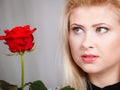 Woman holding red rose near face looking melancholic