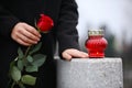 Woman holding red rose near grey granite tombstone with candle outdoors, closeup. Funeral ceremony Royalty Free Stock Photo