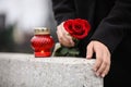 Woman holding red rose near grey granite tombstone with candle outdoors. Funeral ceremony Royalty Free Stock Photo