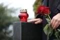 Woman holding red roses near black granite tombstone with candle outdoors, closeup. Funeral ceremony Royalty Free Stock Photo