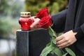 Woman holding red roses near black granite tombstone with candle outdoors. Funeral ceremony Royalty Free Stock Photo