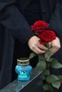 Woman holding red roses near granite tombstone with candle outdoors, closeup. Funeral ceremony Royalty Free Stock Photo