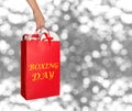 Woman holding red shopping bag with text Boxing Day full of gifts on blurred silver background. Space for text Royalty Free Stock Photo