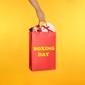 Woman holding red shopping bag with text Boxing Day full of gifts on yellow background Royalty Free Stock Photo