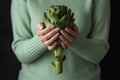 Woman holding ripe organic artichoke on dark background. Vegetable concept